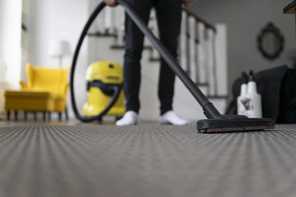 vacuuming gray patterned carpet in modern living room with yellow armchair